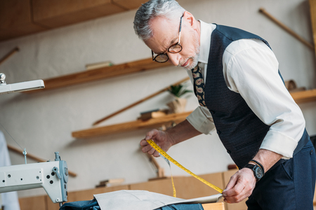handsome tailor measuring cloth with tape measure at sewing workshopの写真素材