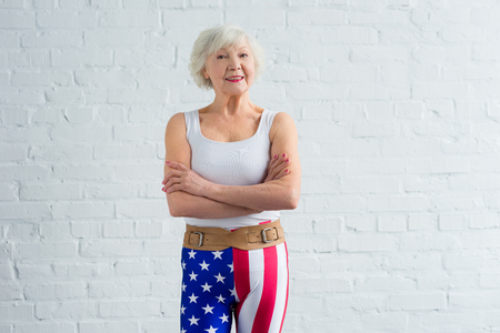 happy senior woman in sportswear standing with crossed arms and smiling at cameraの写真素材