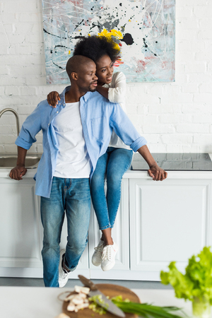 happy african american woman hugging husband in kitchen at homeの写真素材