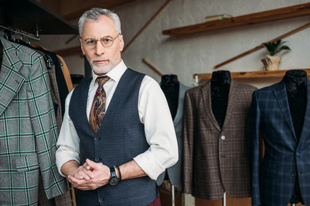 handsome mature tailor looking at camera in sewing workshop