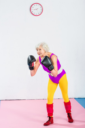 full length view of senior woman in sportswear and boxing gloves training and looking awayの写真素材