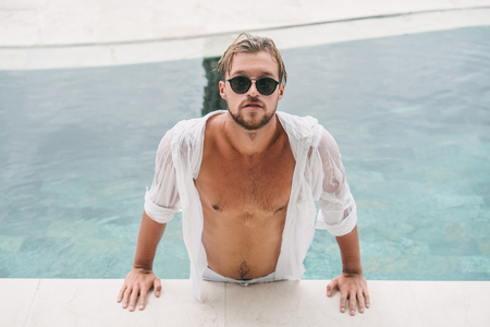 sexy handsome man in sunglasses leaning on poolside in Bali, Indonesiaの写真素材