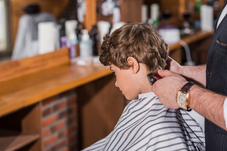 little curly kid getting haircut from barber with Hair Clipperの写真素材