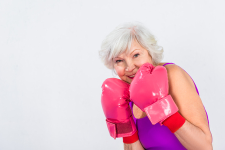 beautiful senior woman in boxing gloves smiling at camera isolated on greyの写真素材