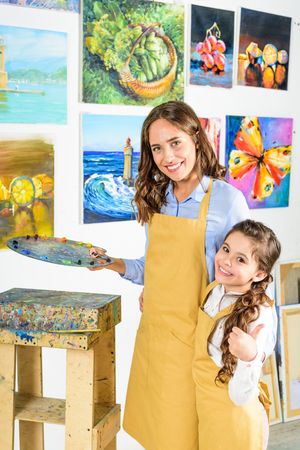 teacher hugging pupil and she showing thumb up in workshop of art schoolの写真素材