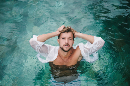 sexy handsome man looking at camera and standing in swimming pool in Bali, Indonesiaの写真素材