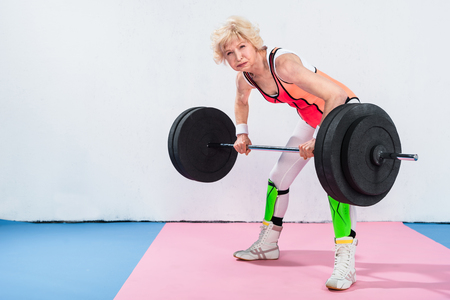 beautiful sportive senior lady lifting barbell and looking at cameraの写真素材