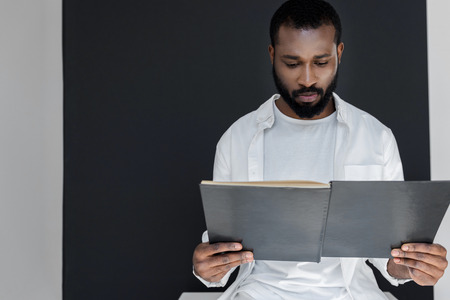 handsome stylish african american man in white clothes reading black book