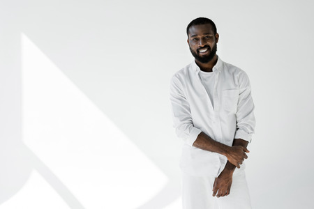 smiling stylish african american man in white clothes looking at camera on white