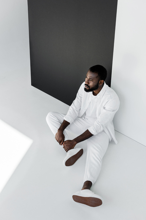 high angle view of handsome stylish african american man sitting on floor in white clothesの写真素材