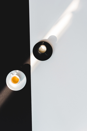 top view of black and white cups of milk and coffee on black and white surfaceの写真素材
