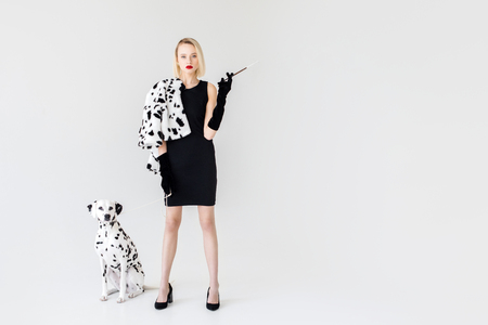 attractive stylish blonde woman in black dress with dalmatian dog on whiteの写真素材