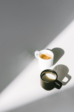 high angle view of black and white cups of milk and coffee on white surfaceの写真素材
