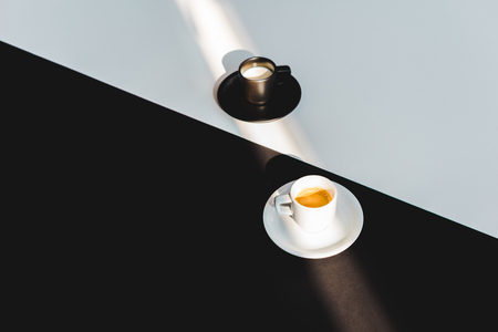 high angle view of black and white cups of milk and coffee on black and white surface, yin yang conceptの写真素材