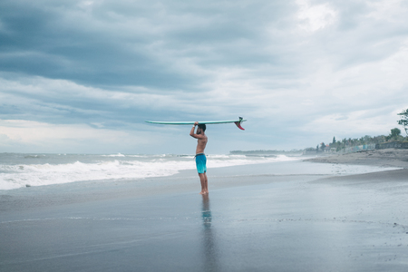 surfer holding surfboard on head and looking at ocean in Bali, Indonesiaの写真素材