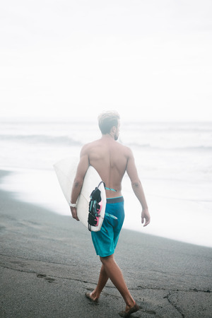 rear view of surfer walking with surfboard in Bali, Indonesiaの写真素材