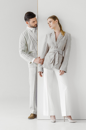 fashionable young man in vintage jacket touching his girlfriend from behind white wallの写真素材