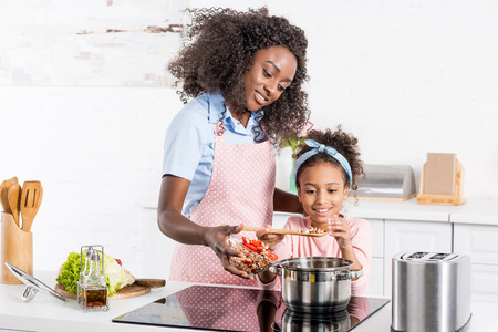 african american mom and daughter cooking on electric stove togetherの写真素材