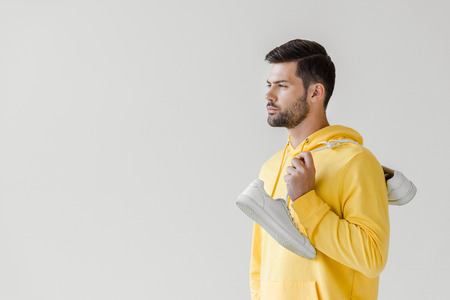 handsome young man in yellow hoodie with white sneakers hanging on shoulder isolated on whiteの写真素材