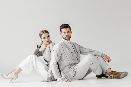 couple of attractive models in vintage clothes sitting on floor and leaning back to back on whiteの写真素材
