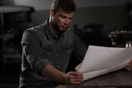 young male worker sitting and looking at blueprint