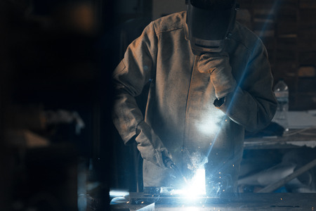 welder in protection mask working with metal at factory