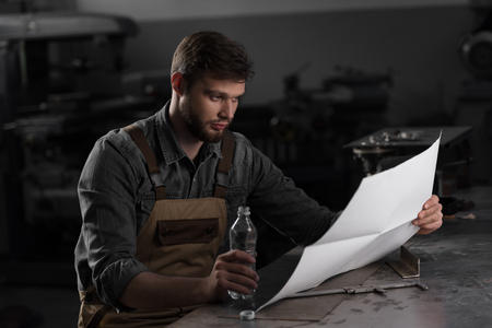 workman sitting with bottle of water and looking at blueprintの写真素材