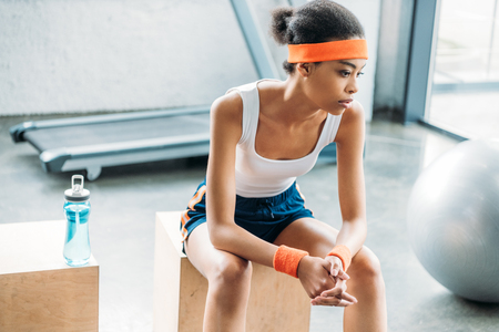 attractive african american sportswoman in headband and headbands resting on wooden box at gymの写真素材
