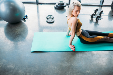 side view of young athletic woman resting on fitness mat after work out at gymの写真素材
