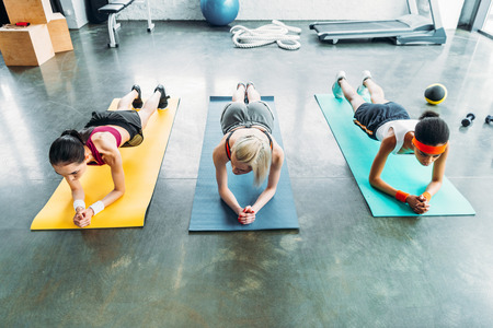 three young multicultural sportswomen doing plank at gymの写真素材