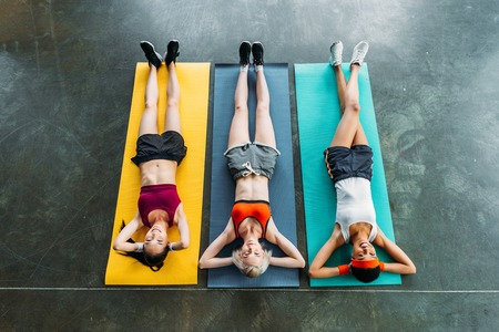 high angle view of three multiethnic sportswomen on fitness mats at gymの写真素材