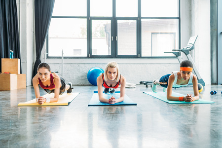 front view of multiethnic female athletes doing plank on fitness mats at gymの写真素材