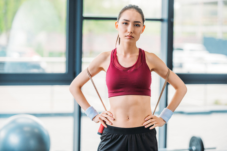 portrait of young asian sportswoman with skipping rope looking at camera at gymの写真素材