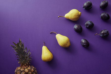 top view of pears, plums and pineapple on violet surfaceの写真素材