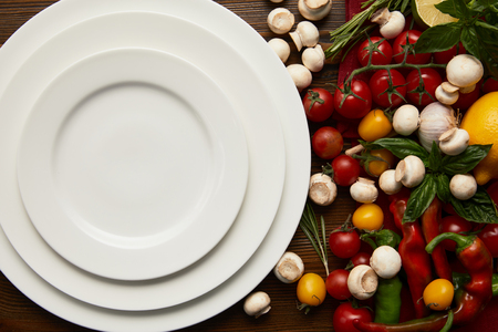 top view of empty round white plates and fresh vegetables on wooden surfaceの写真素材