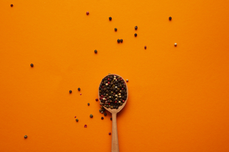 top view of wooden spoon with peppercorns on orange backgroundの写真素材