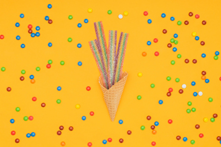 top view of flat jelly candies in waffle cone and scattered dragee isolated on orangeの写真素材