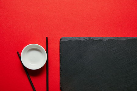 top view of arranged empty bowl, chopsticks and slate plate on red backgroundの写真素材
