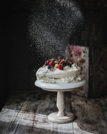 white pie with berries on cake stand on wooden tableの写真素材