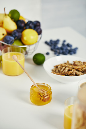 close up view of honey, fresh fruits and glass of juice for breakfast on white surfaceの写真素材