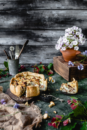 yummy pie with mushrooms and potted flowers on wooden tableの写真素材