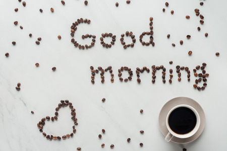 top view of cup of coffee and good morning lettering made of coffee beans on white marbleの写真素材