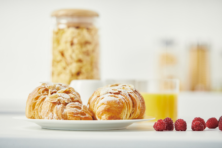 close up view of freshly baked croissants and raspberries for breakfast on white surfaceの写真素材