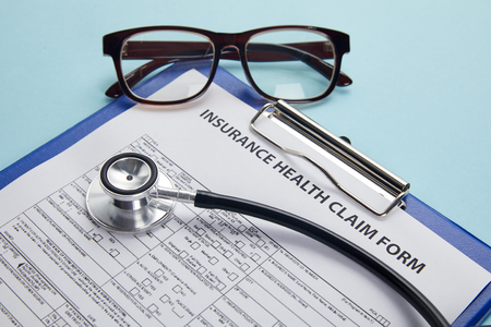 insurance health claim form, clipboard, eyeglasses and stethoscope on blueの写真素材