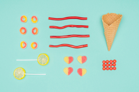 flat lay of jelly candies, dragee, lollipops and waffle cone isolated on turquoiseの写真素材