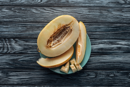 top view of sweet ripe sliced melon on plate on wooden surface
