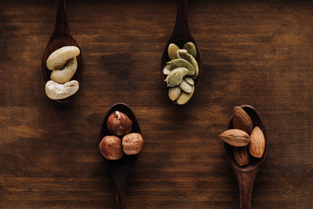 variety of nuts in dark spoons on wooden surface