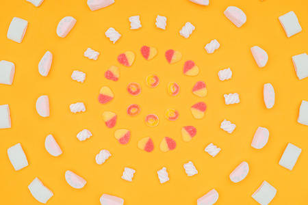 top view of circles of yummy jelly candies and marshmallows isolated on orange