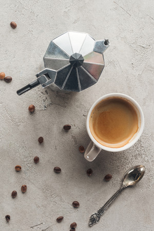 top view of cup of delicious coffee and moka pot on concrete surface with spilled coffee beansの写真素材