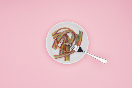top view of flat colored jelly candies with sugar and fork on plate isolated on pinkの写真素材